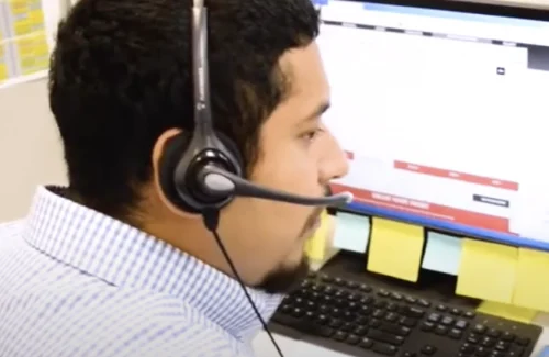 Man on phone headset in working environment looking at laptop screen showing call tracking analytics.
