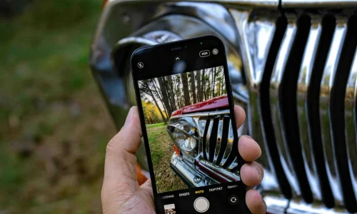 man holding a phone in his hand and taking a picture of a car