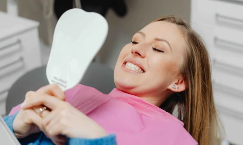 woman looking at her teeth in the mirror in a dental office